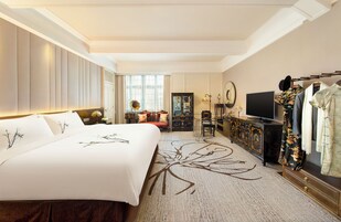 A hotel room with a large bed, a TV, a wardrobe, and a desk with a lamp.