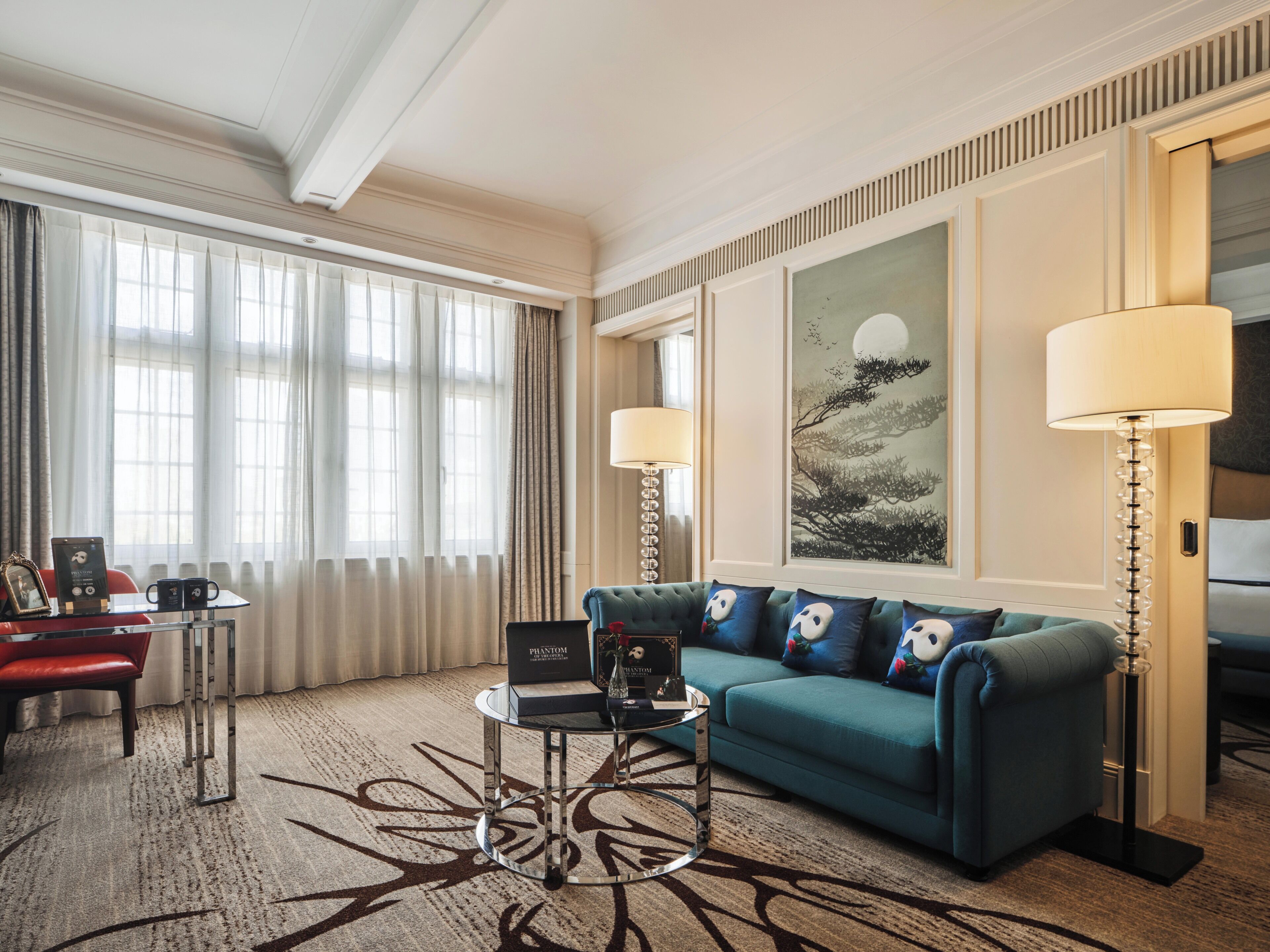 A hotel room with a sofa, a coffee table, a lamp, and a painting on the wall.