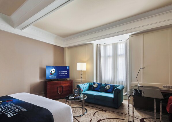 Habitación de hotel con cama, sofá azul, televisor, escritorio y lámpara.
