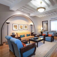 A spacious living room with a high ceiling, a sofa set, armchairs, a coffee table, and a fireplace.