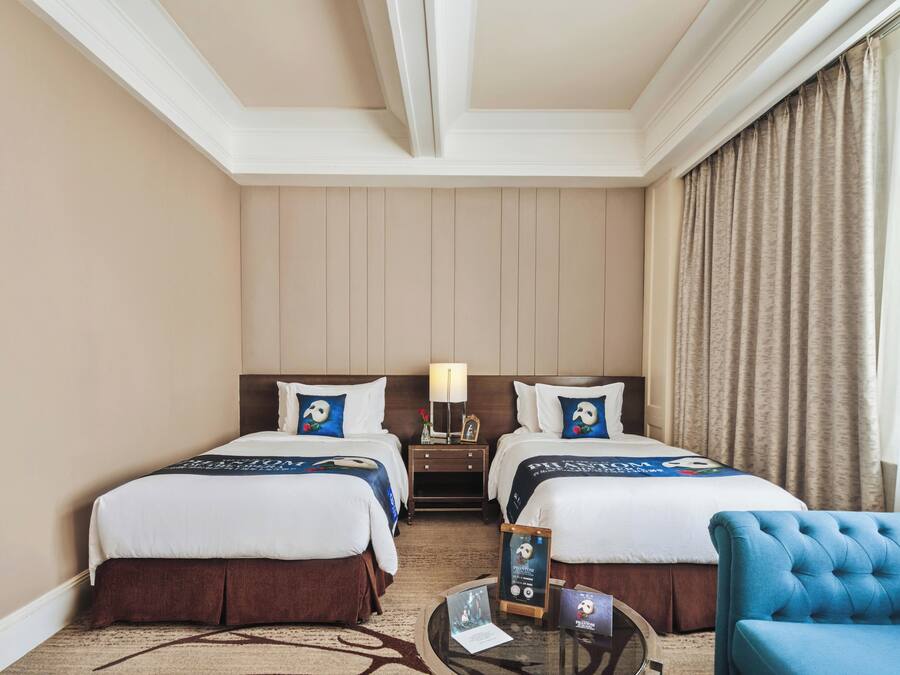 A hotel room with two beds, a nightstand, a blue armchair, and a carpeted floor.