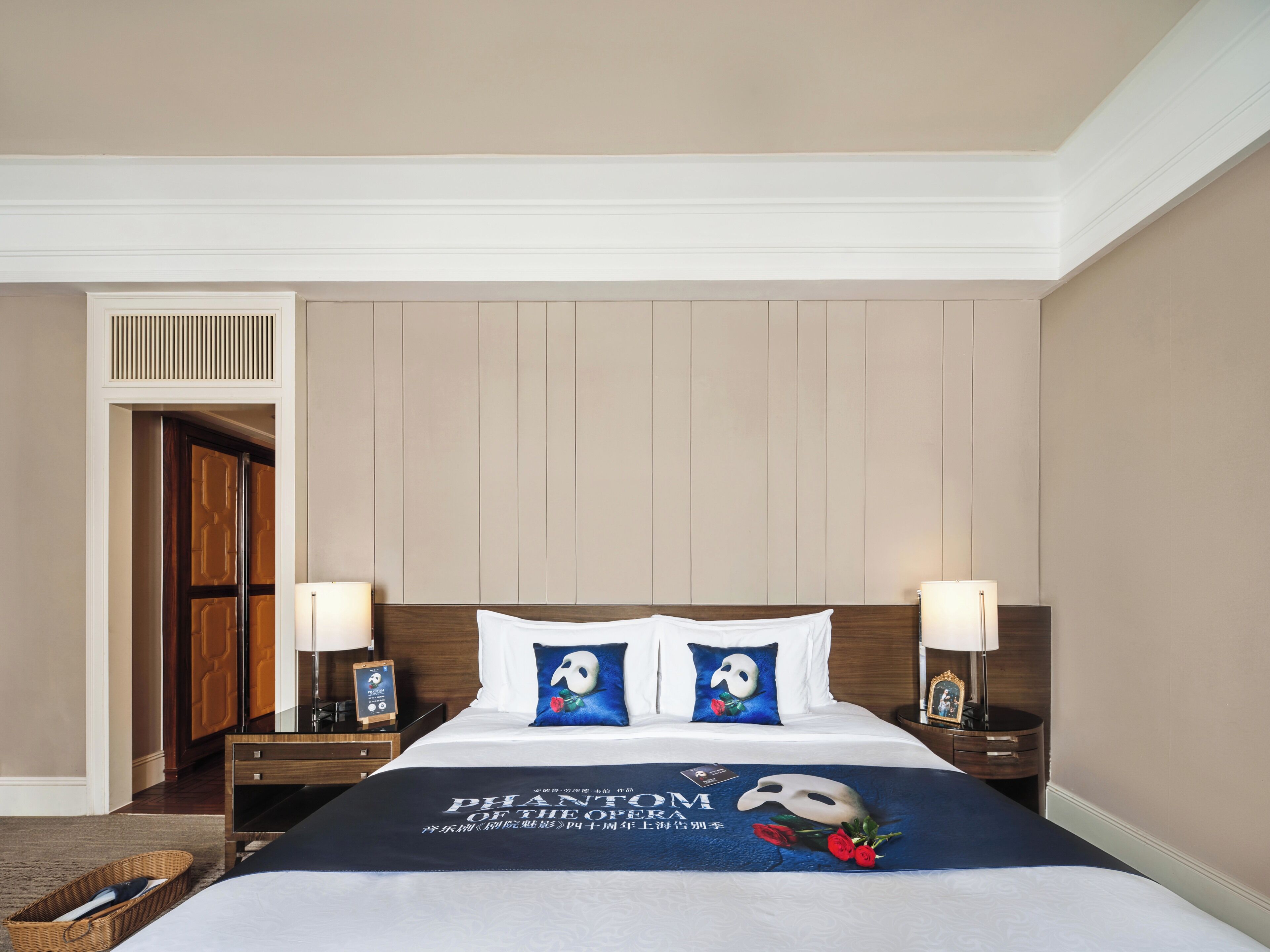 Une chambre d’hôtel avec un lit, deux tables de chevet, une commode et une porte.