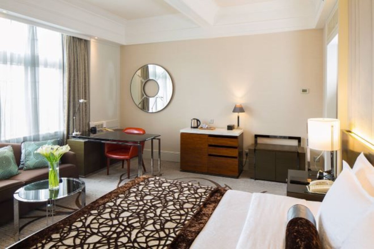Quarto de hotel com uma cama, escrivaninha, cadeira, sofá, cafeteira e um espelho na parede.