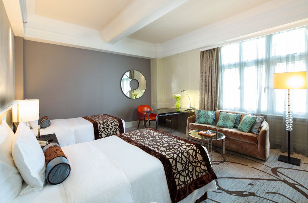 Una habitación de hotel con dos camas, un sofá, un escritorio y una lámpara.