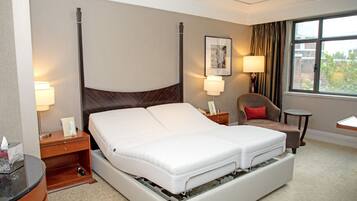 A hotel room with a large bed, two bedside tables, a chair, a small table, a lamp, a picture on the wall, and a window with curtains.