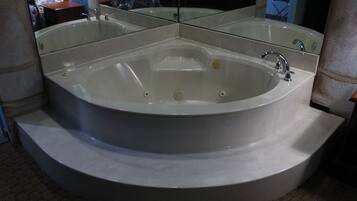 A large, freestanding bathtub with a curved design, positioned in a corner of a room with a tiled floor.