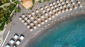 An aerial view of a beach with rows of sun loungers and umbrellas, a thatched-roof structure, and a clear blue sea. - Out Of The Blue All Inclusive Resort & Spa (Malevizi)