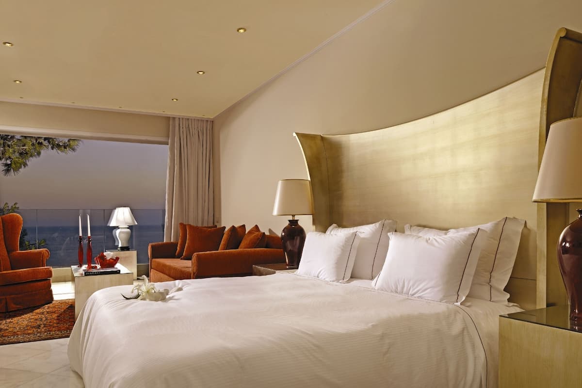 Une chambre d’hôtel spacieuse, dotée d’un grand lit, de deux fauteuils, d’une table de chevet et offrant une vue sur l’extérieur.