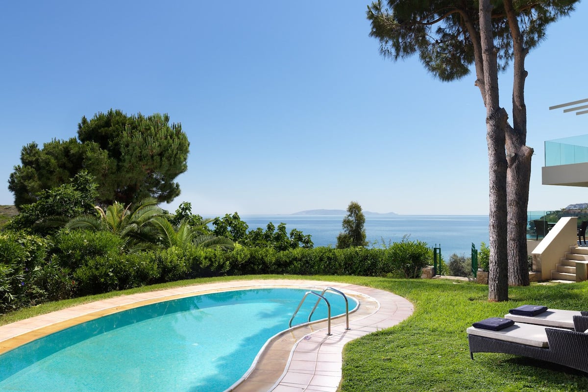 Une piscine à bord incurvé, entourée d’une végétation luxuriante et offrant une vue sur la mer.