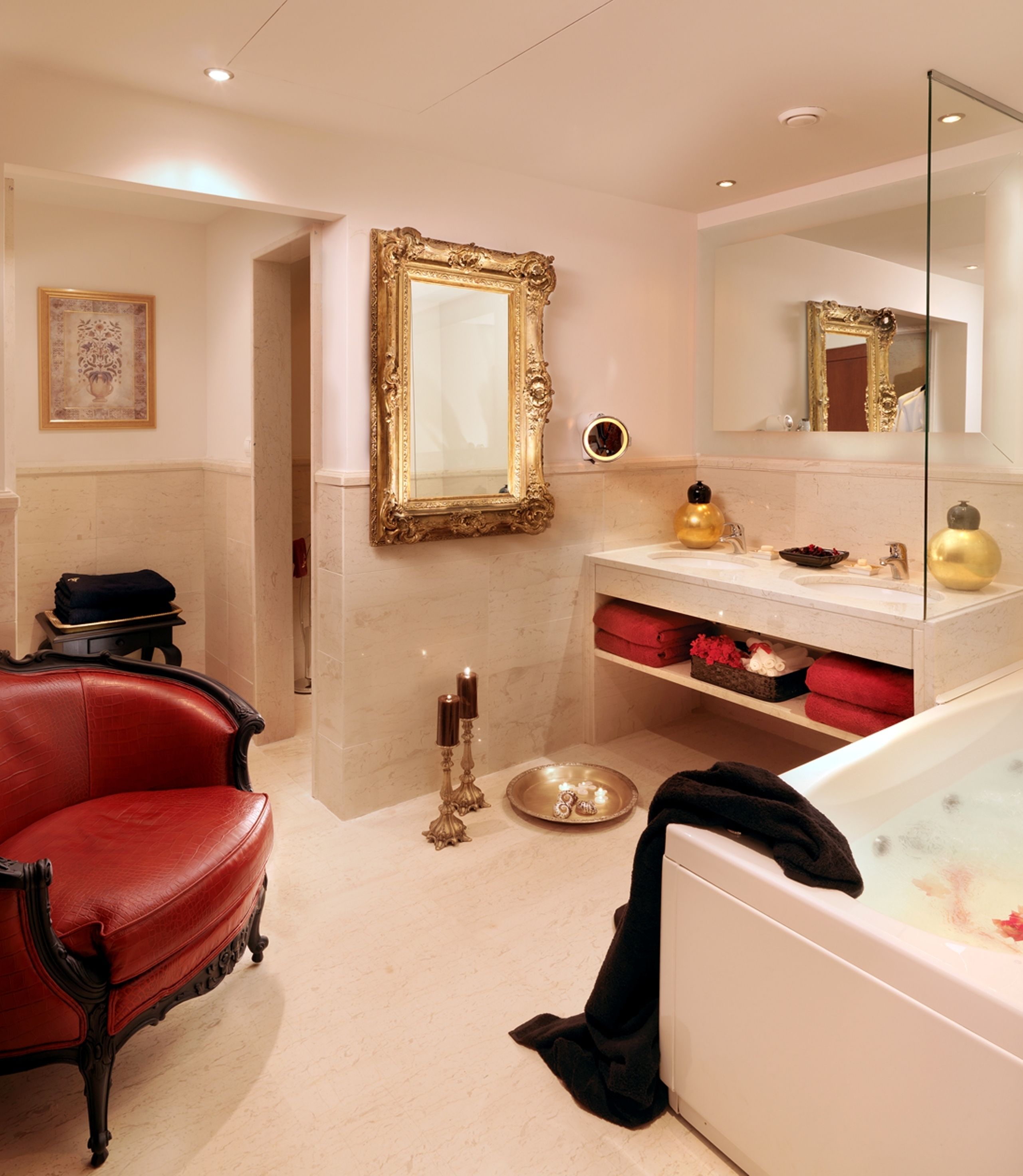 A bathroom with a red leather chair, a gold-framed mirror, a bathtub, and a vanity with a gold soap dispenser.