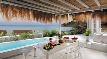 Un comedor con vista al mar, una piscina y un techo de paja.