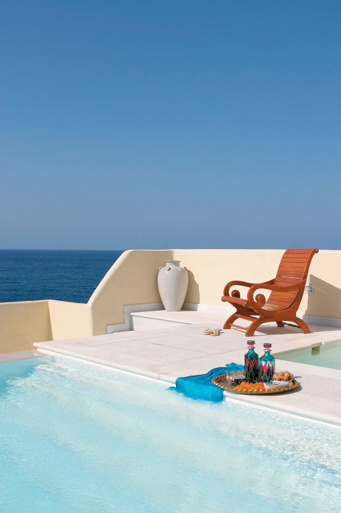 A poolside area with a wooden chair, a vase, and a tray with bottles and snacks.