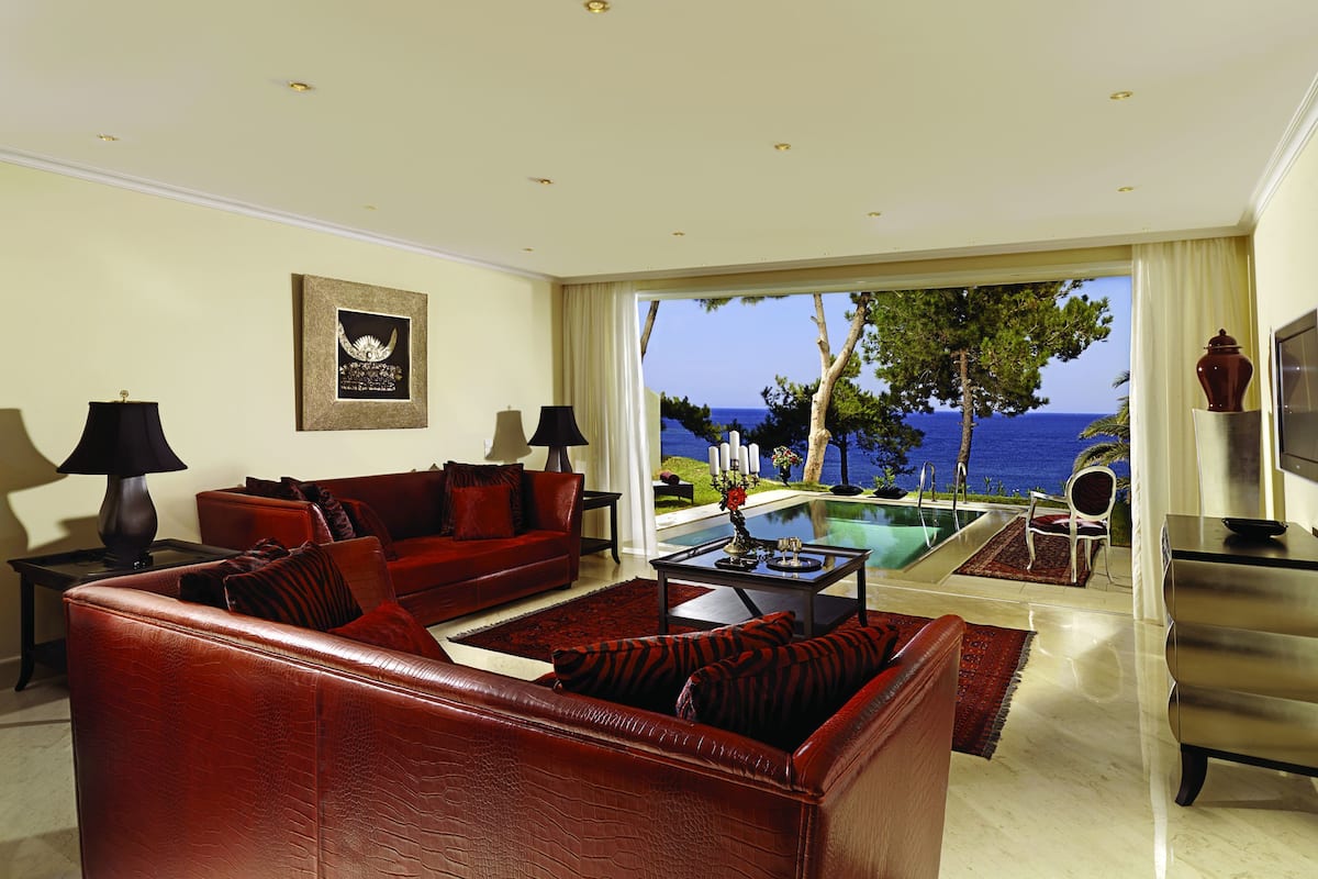 Un salon spacieux avec un canapé en cuir rouge, une table basse en verre et une vue sur la mer grâce à de grandes fenêtres.