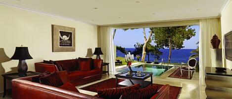 A spacious living room with a red leather sofa, a glass coffee table, and a view of the sea through large windows.