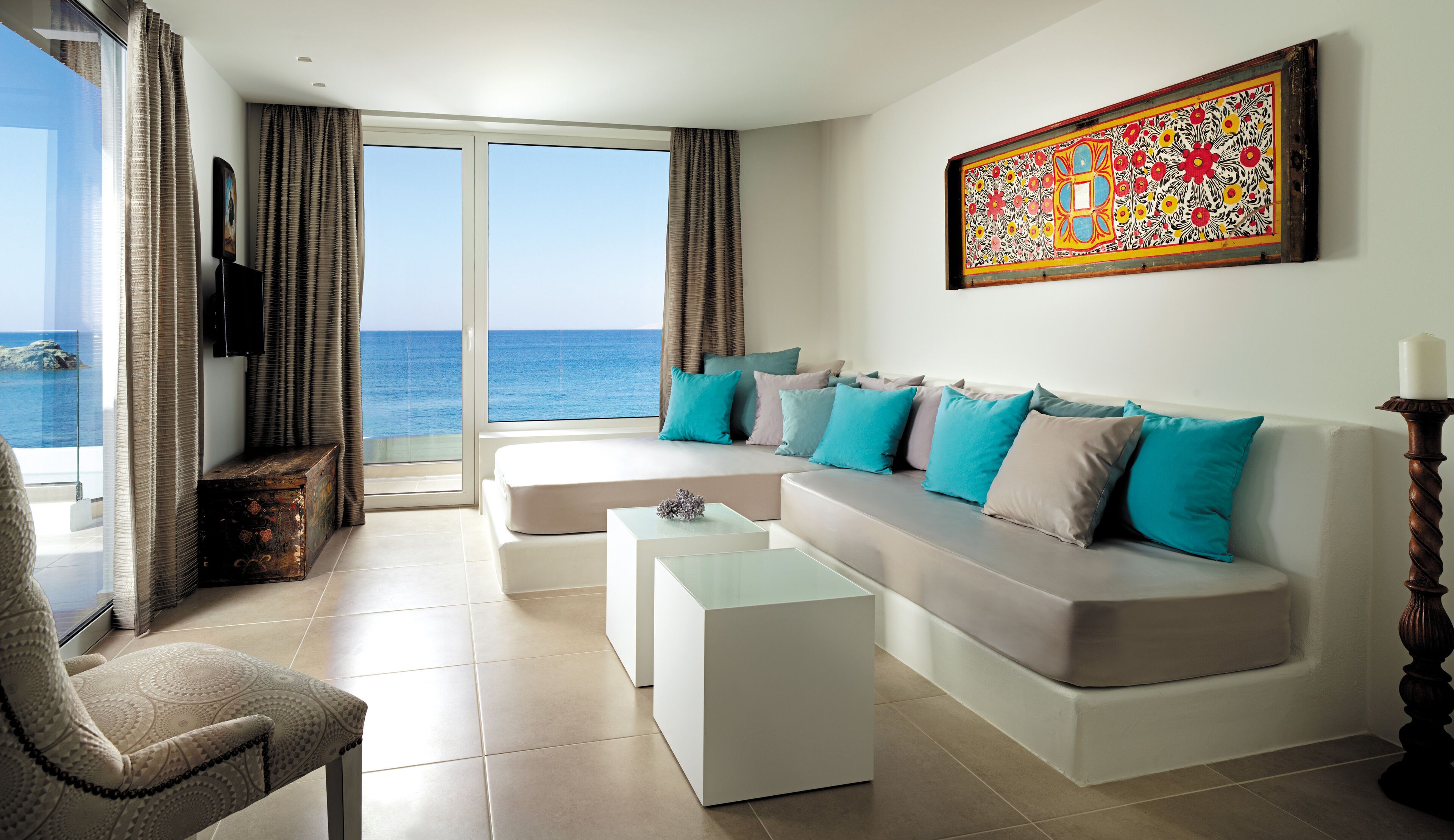 A modern living room with a large sofa, a coffee table, and a view of the sea through large windows.