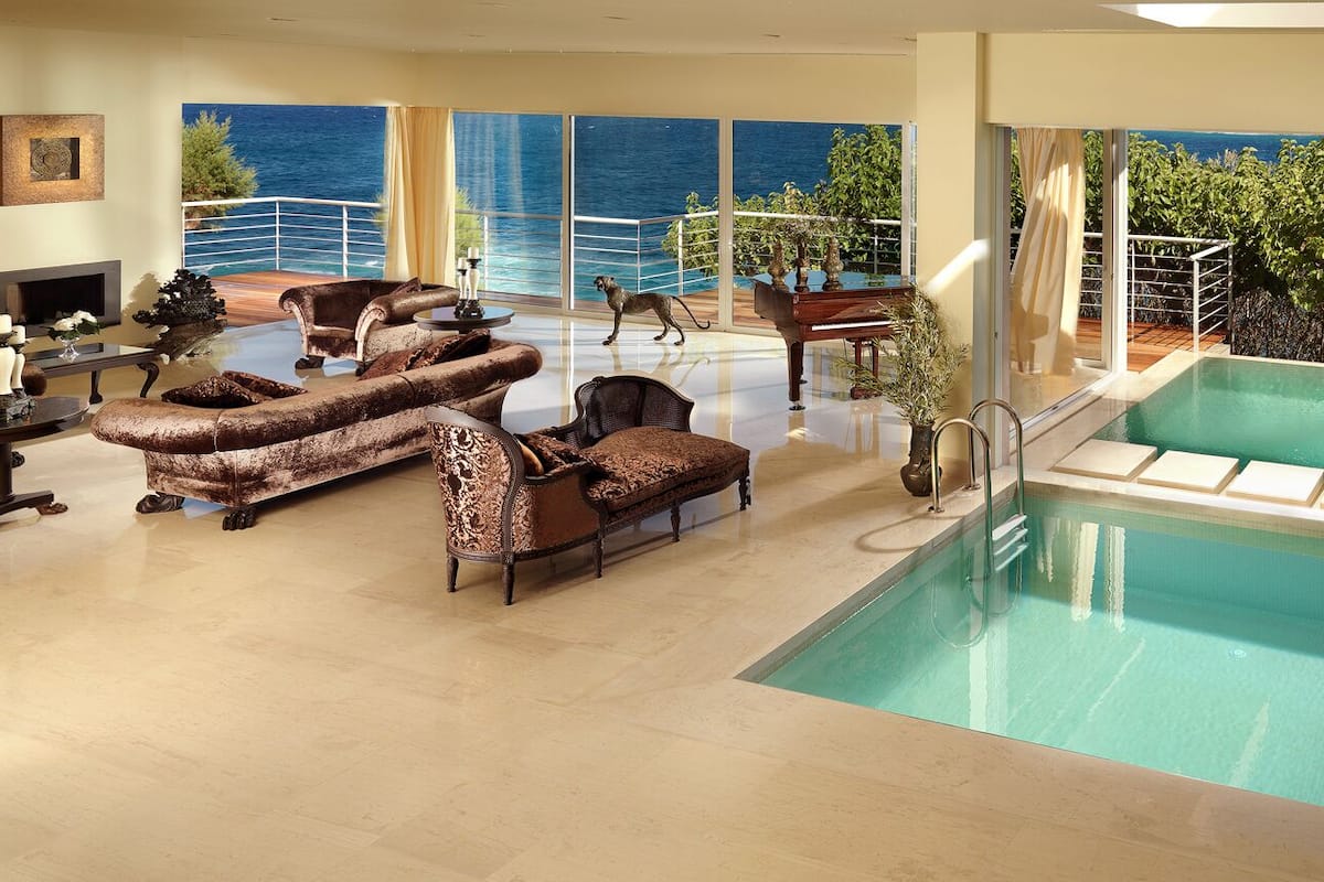 Un espace piscine intérieur luxueux, avec vue sur la mer, aménagé avec des canapés et un piano.
