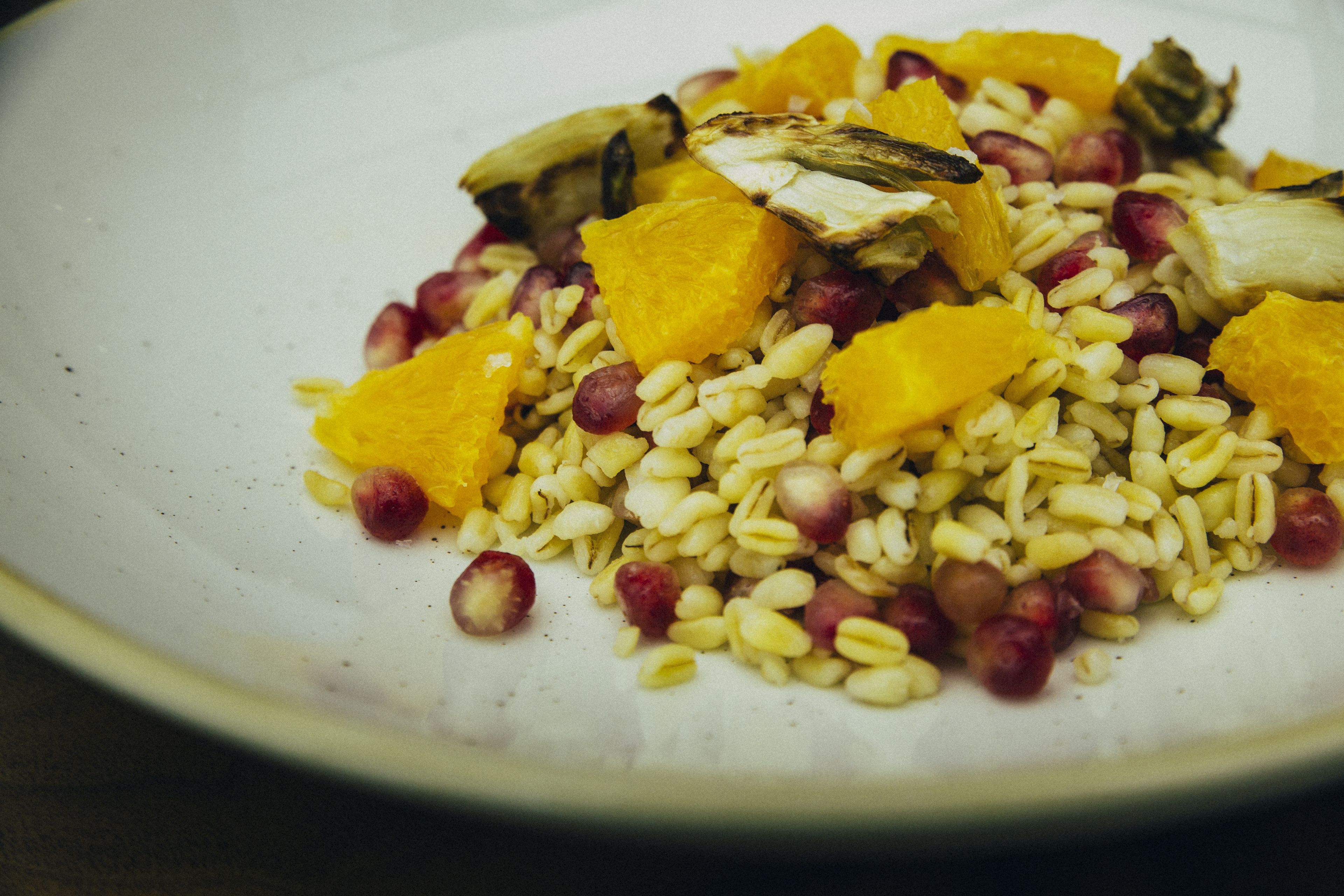 Un plato de comida con granos, semillas de granada y trozos de naranja.