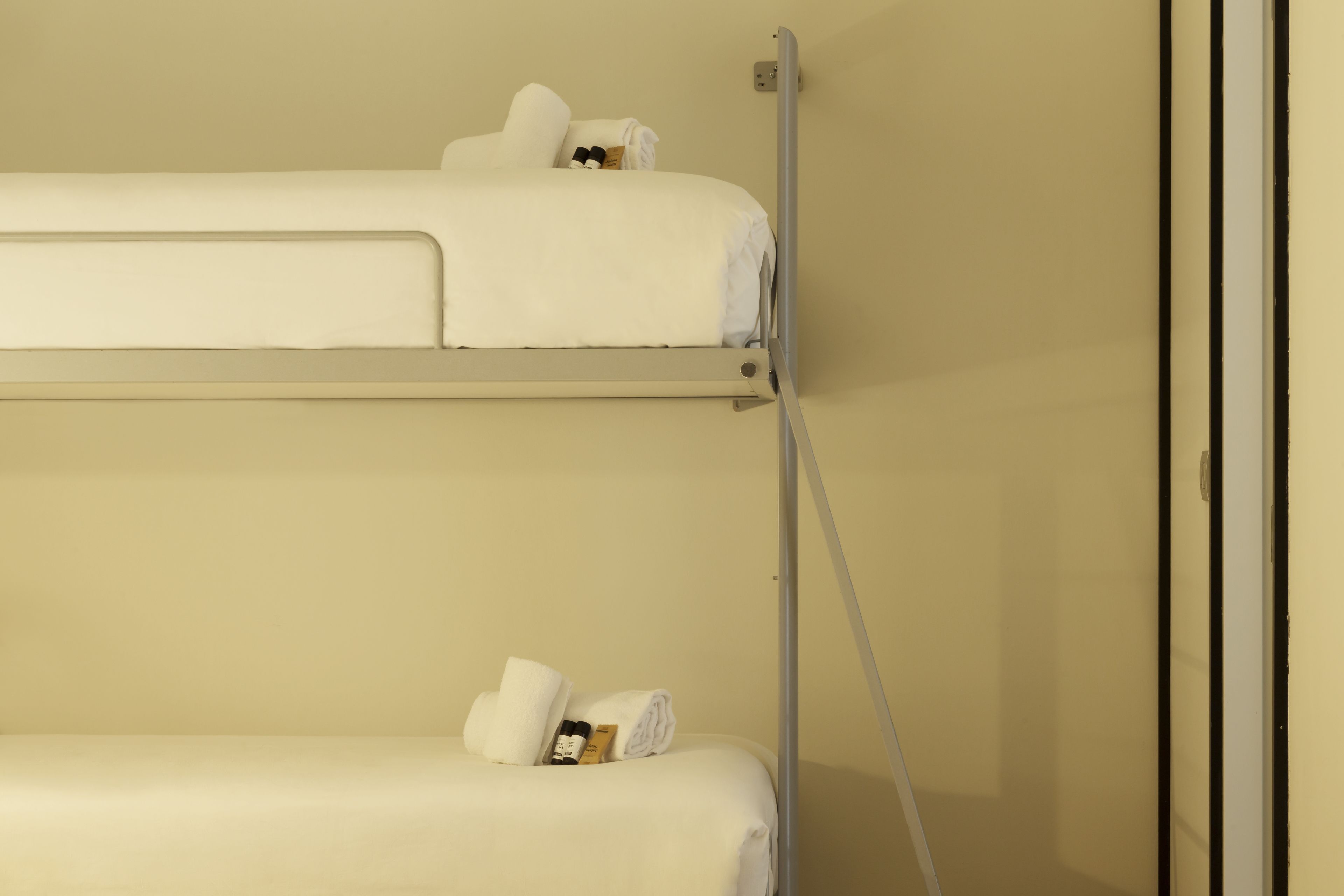 A bunk bed with white bedding and a small bedside table with a bottle and a book.
