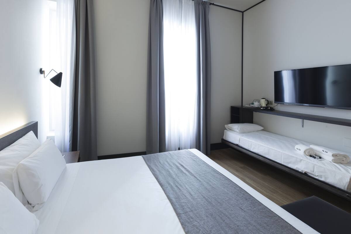 Una habitación de hotel moderna con una cama grande, un televisor montado en la pared y un escritorio pequeño con una lámpara.