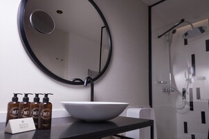 A bathroom with a round mirror, a white sink, and a shower.