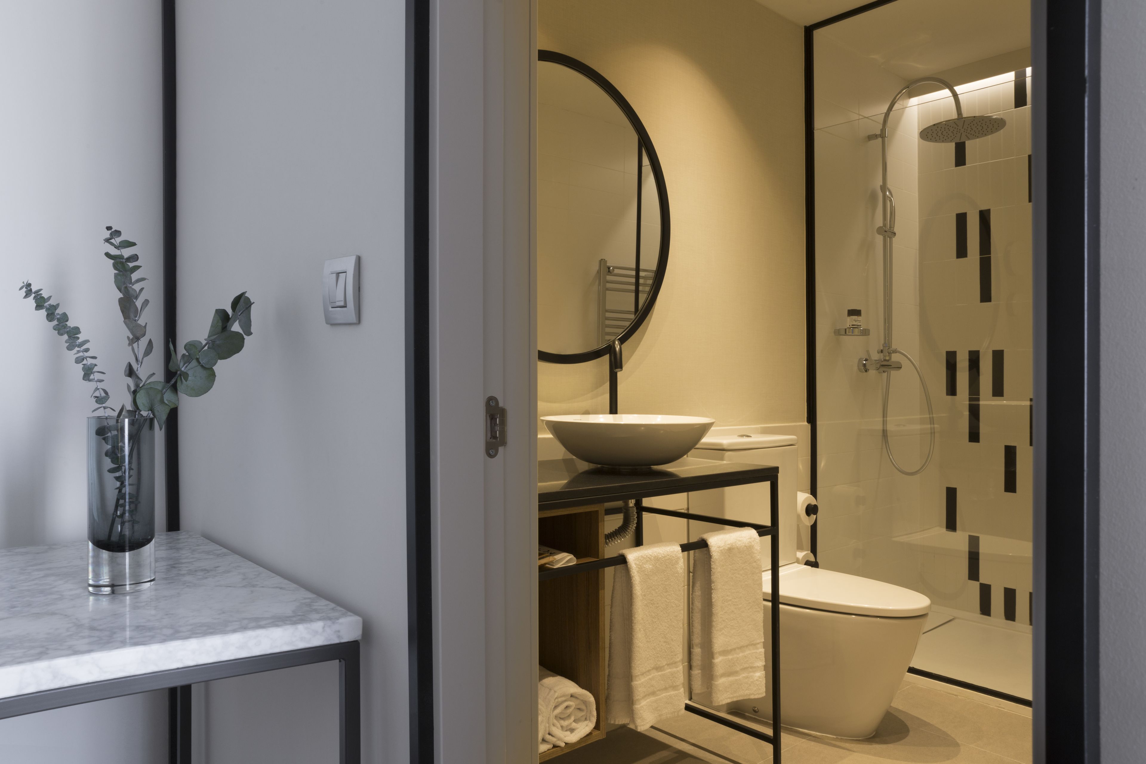 Un baño moderno con ducha de vidrio, un lavabo blanco con recipiente y encimera de mármol.