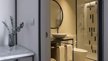 Un baño moderno con ducha de vidrio, un lavabo blanco con recipiente y encimera de mármol.