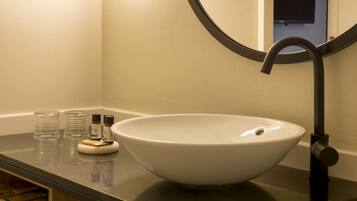A bathroom with a large white sink, a black faucet, and a mirror above the sink. There are two small bottles on the counter.