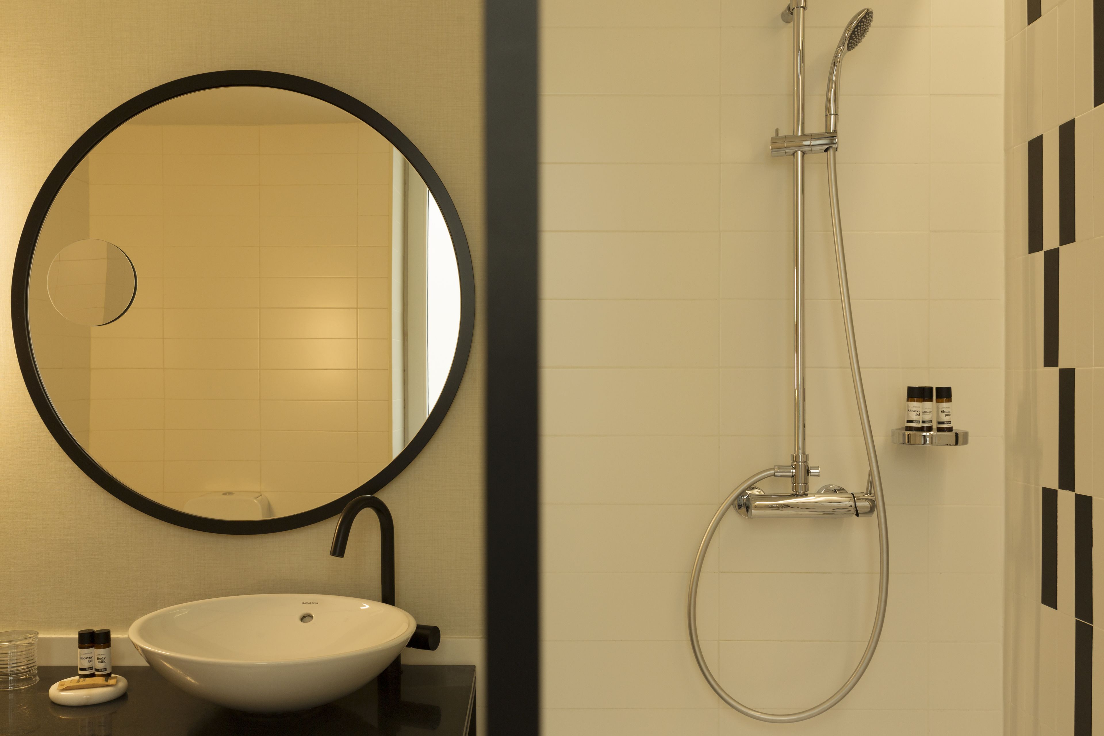 Un baño con un espejo redondo, un lavabo blanco y una ducha con cabezal de ducha manual.