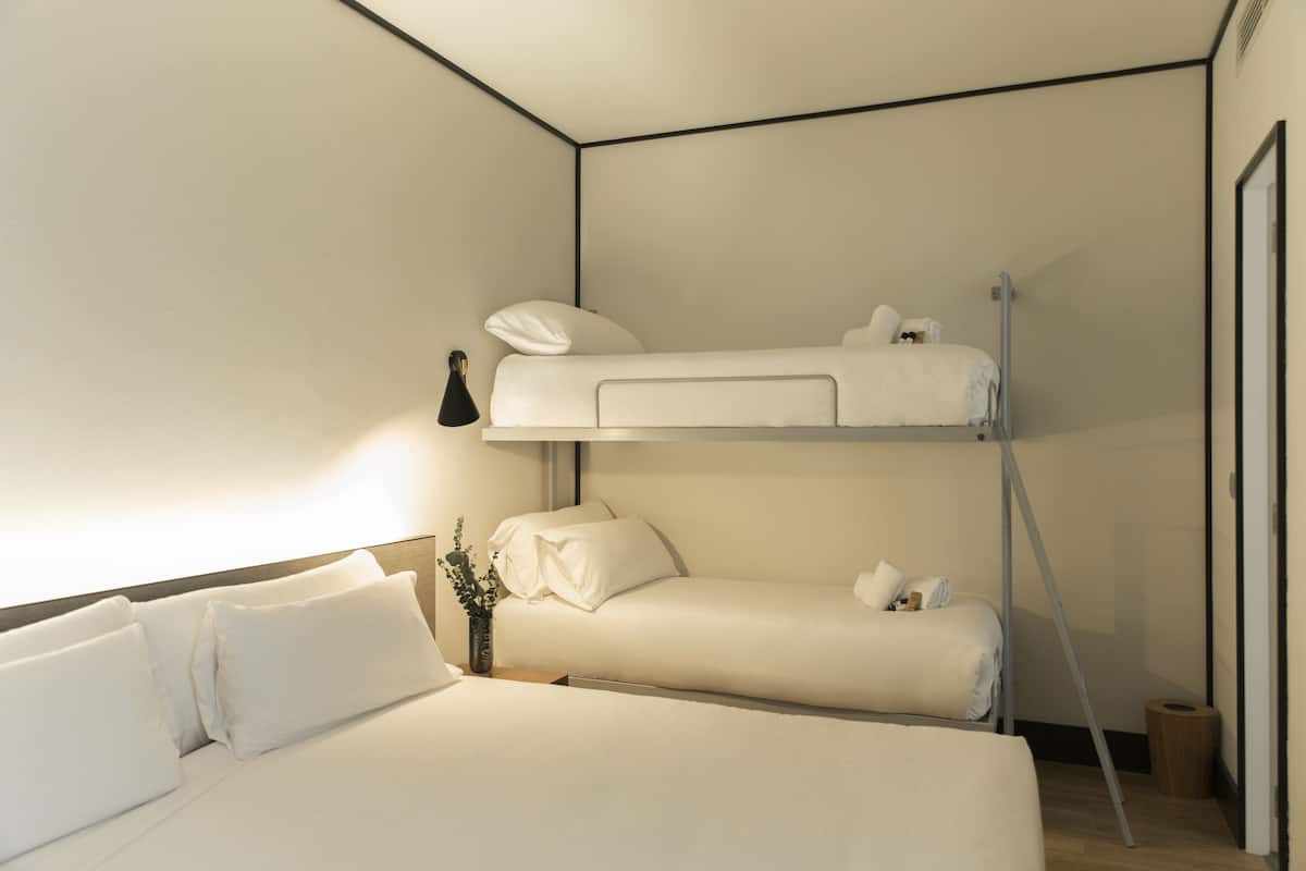 Una habitación de hotel moderna con una litera, una mesita de noche con lámpara y una pequeña planta.