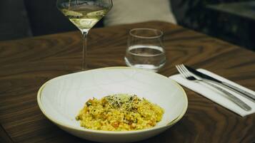 A plate of risotto on a wooden table with a glass of white wine and a water glass.