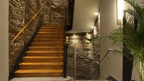 Una escalera de madera con paredes de piedra, barandilla de metal y una planta en maceta.