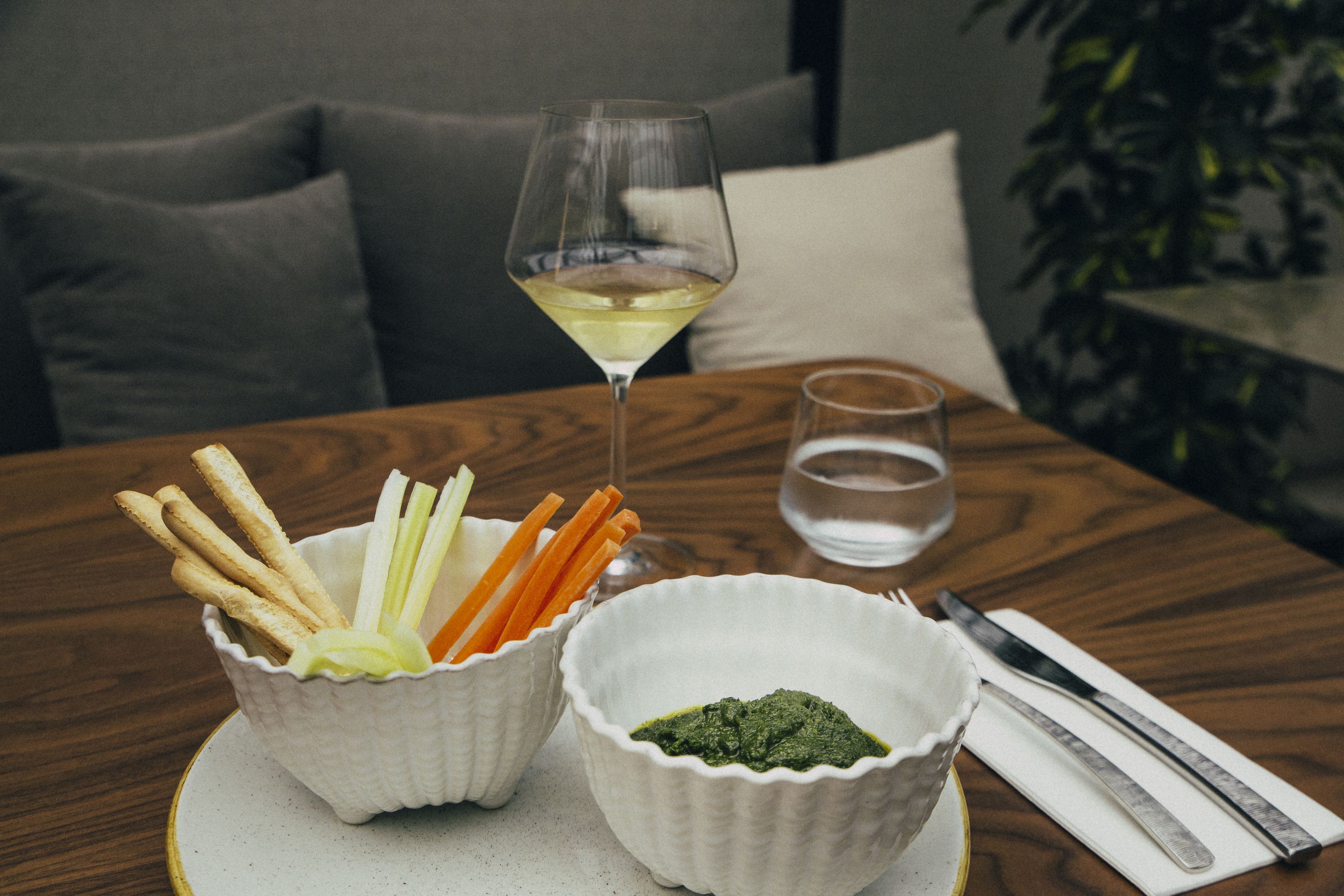 A table with two bowls of snacks, a glass of white wine, and a glass of water.