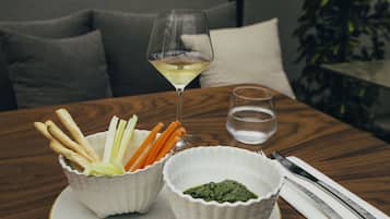 Una mesa con dos cuencos de bocadillos, una copa de vino blanco y un vaso de agua.