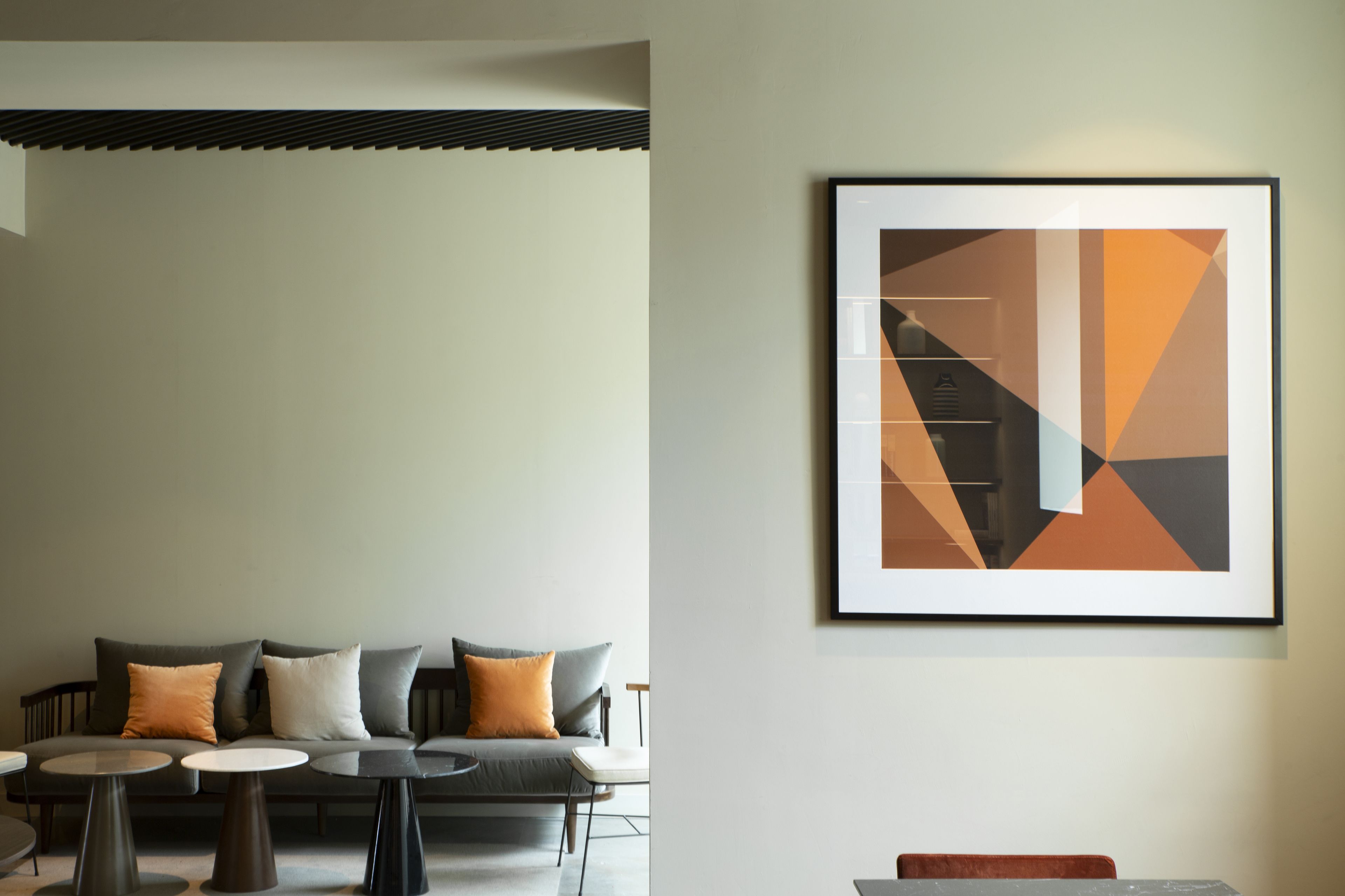 A modern interior with a sofa, two small round tables, and a framed abstract painting on the wall.