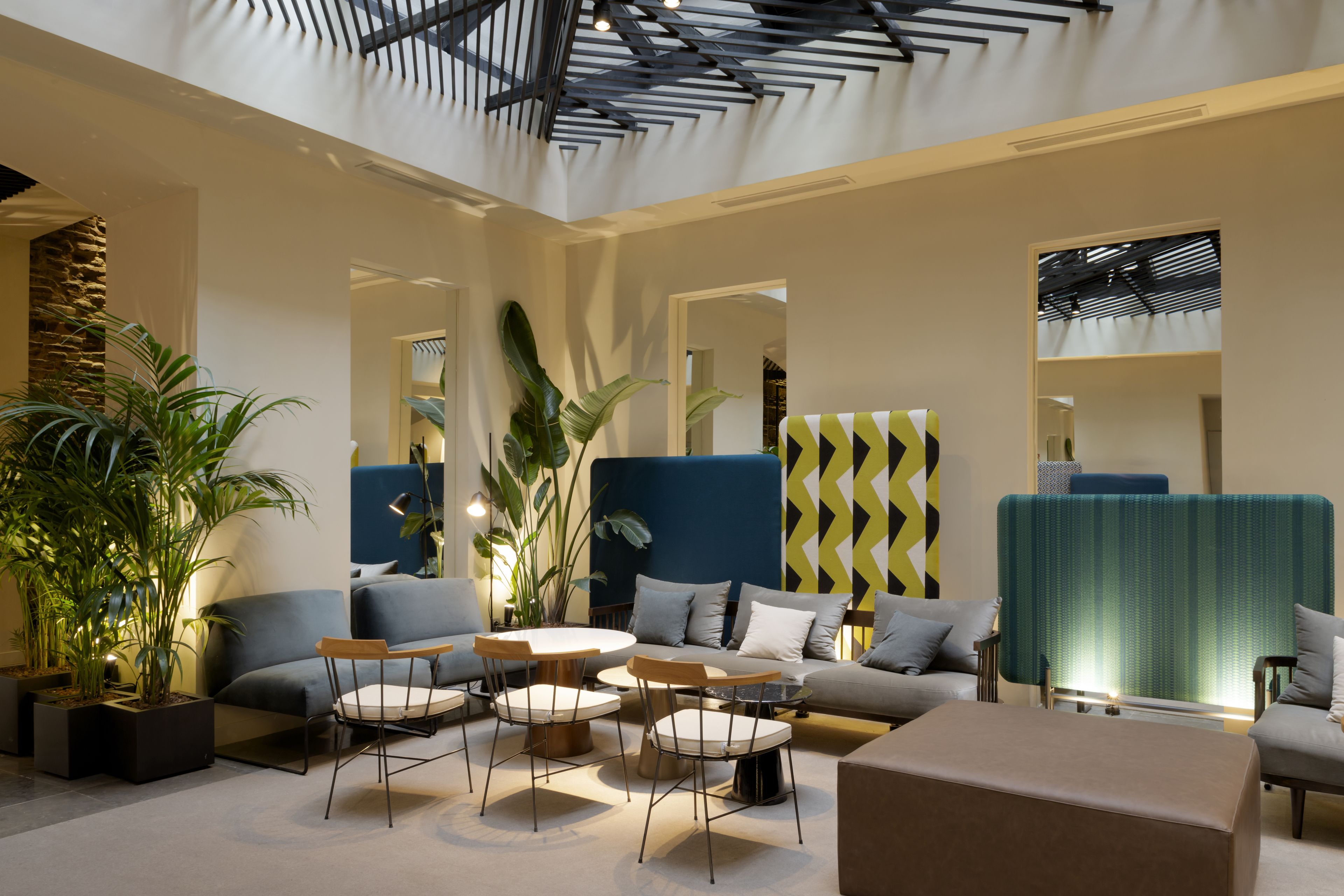 A modern hotel lobby with a high ceiling, seating areas, and potted plants.
