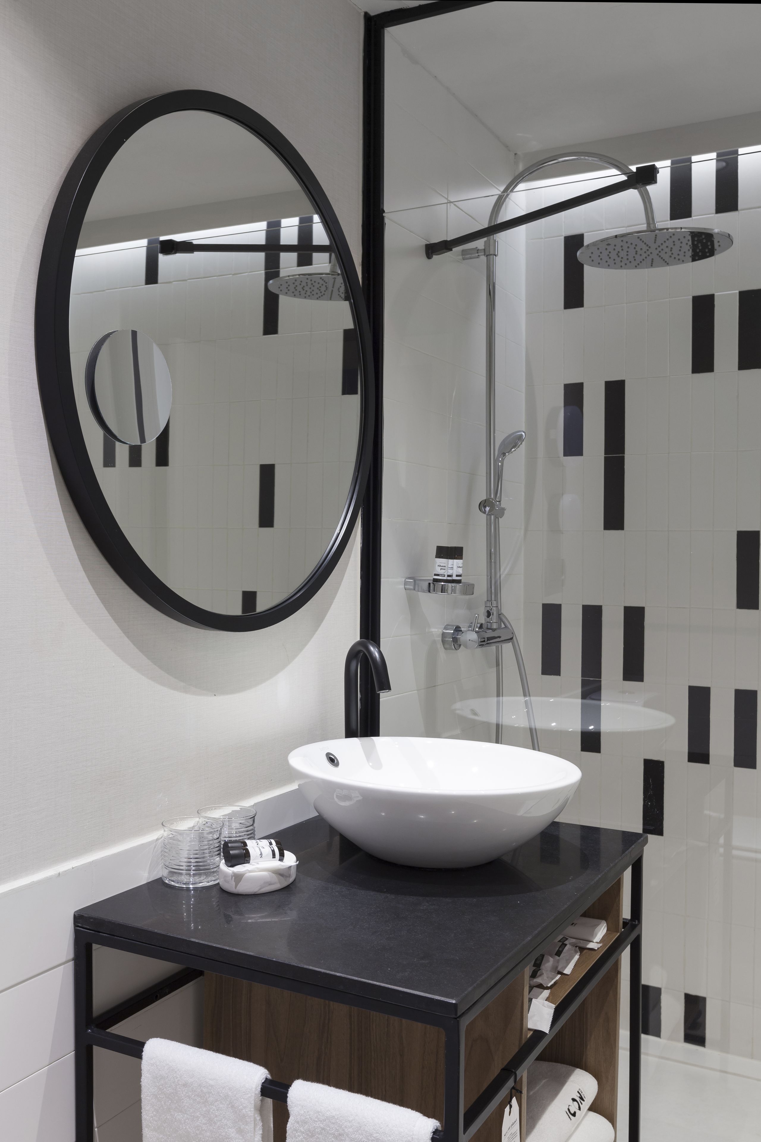 Un baño moderno con un espejo redondo, un lavamanos blanco y una ducha con mampara de vidrio.