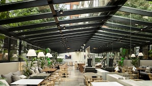 Un café moderno con techos de vidrio, mobiliario de mimbre y plantas de interior.
