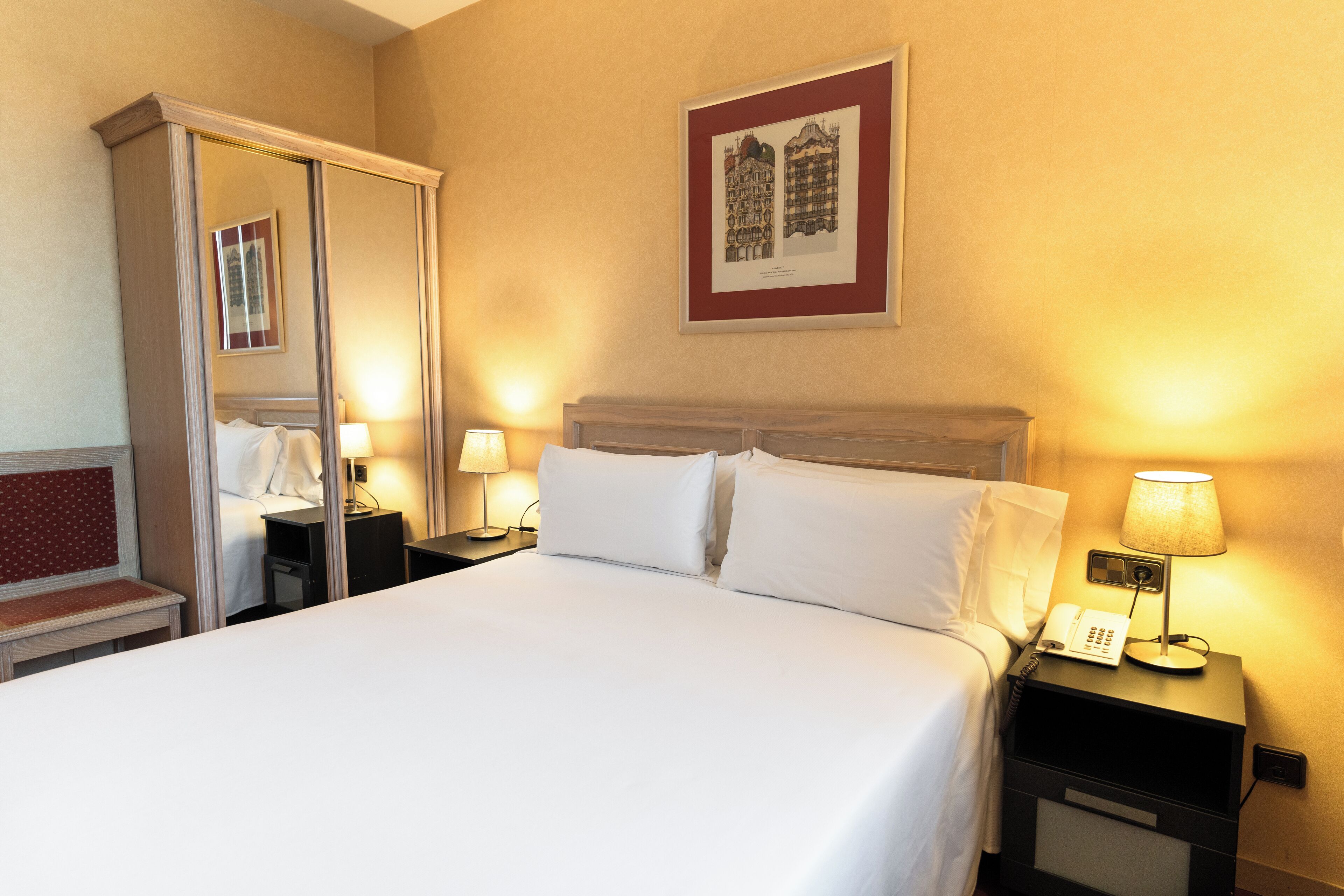 A hotel room with a large bed, two bedside tables, a mirror, and a framed picture on the wall.