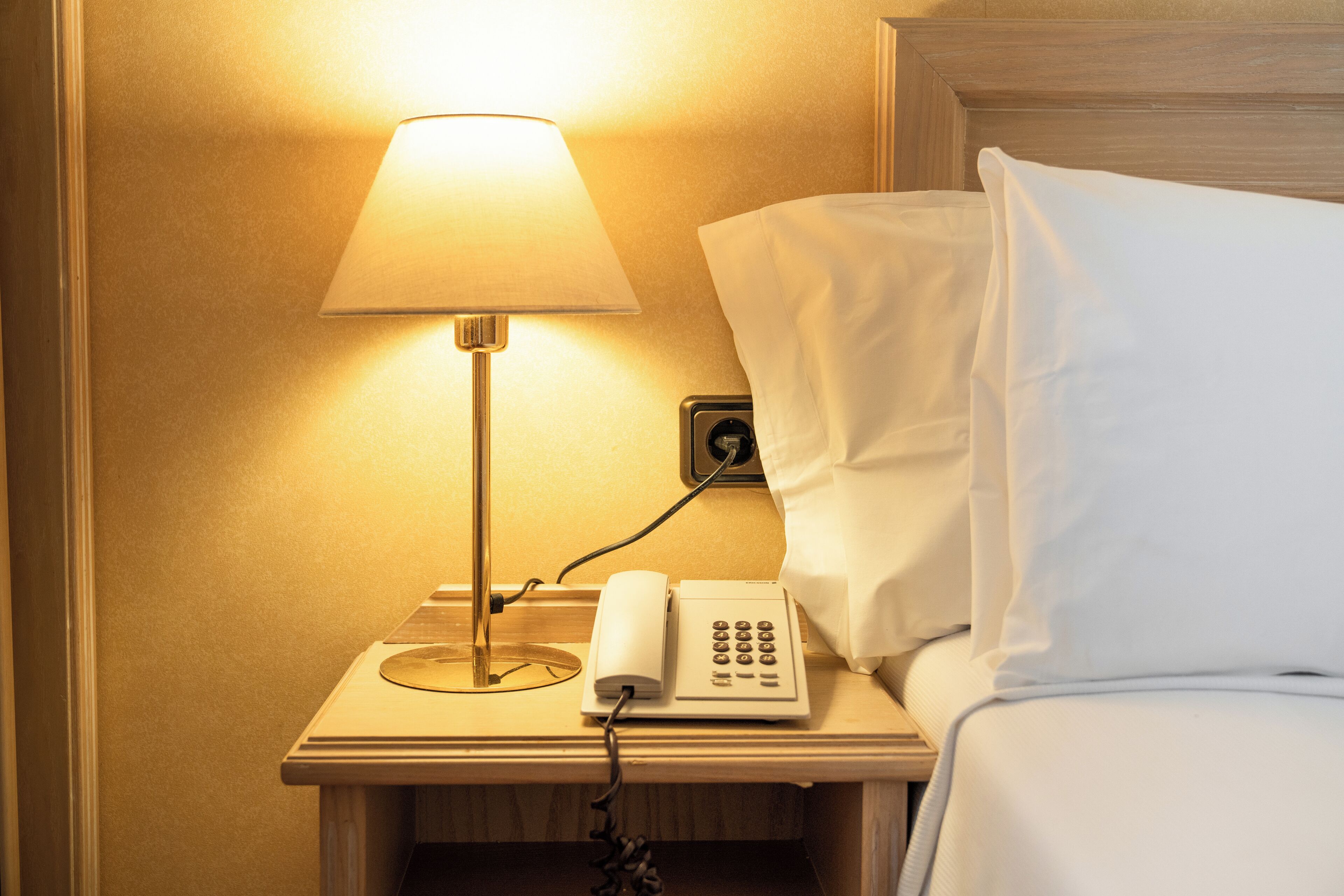 A hotel room with a bedside lamp, a telephone, and a bed with white linens.