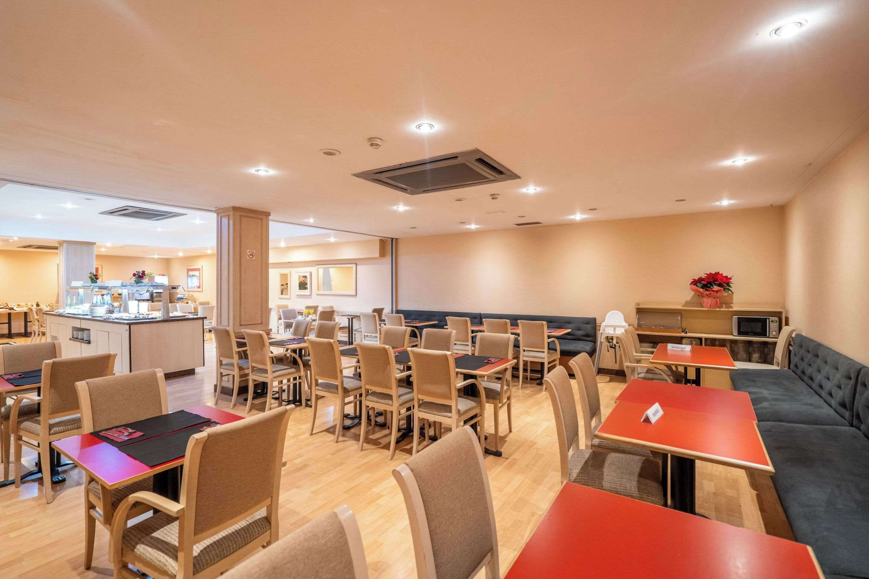 Un comedor amplio con varias mesas y sillas, una barra central y una zona de estar con sofá.