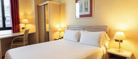 Una habitación de hotel con cama, escritorio, silla y mesita de noche con lámpara.