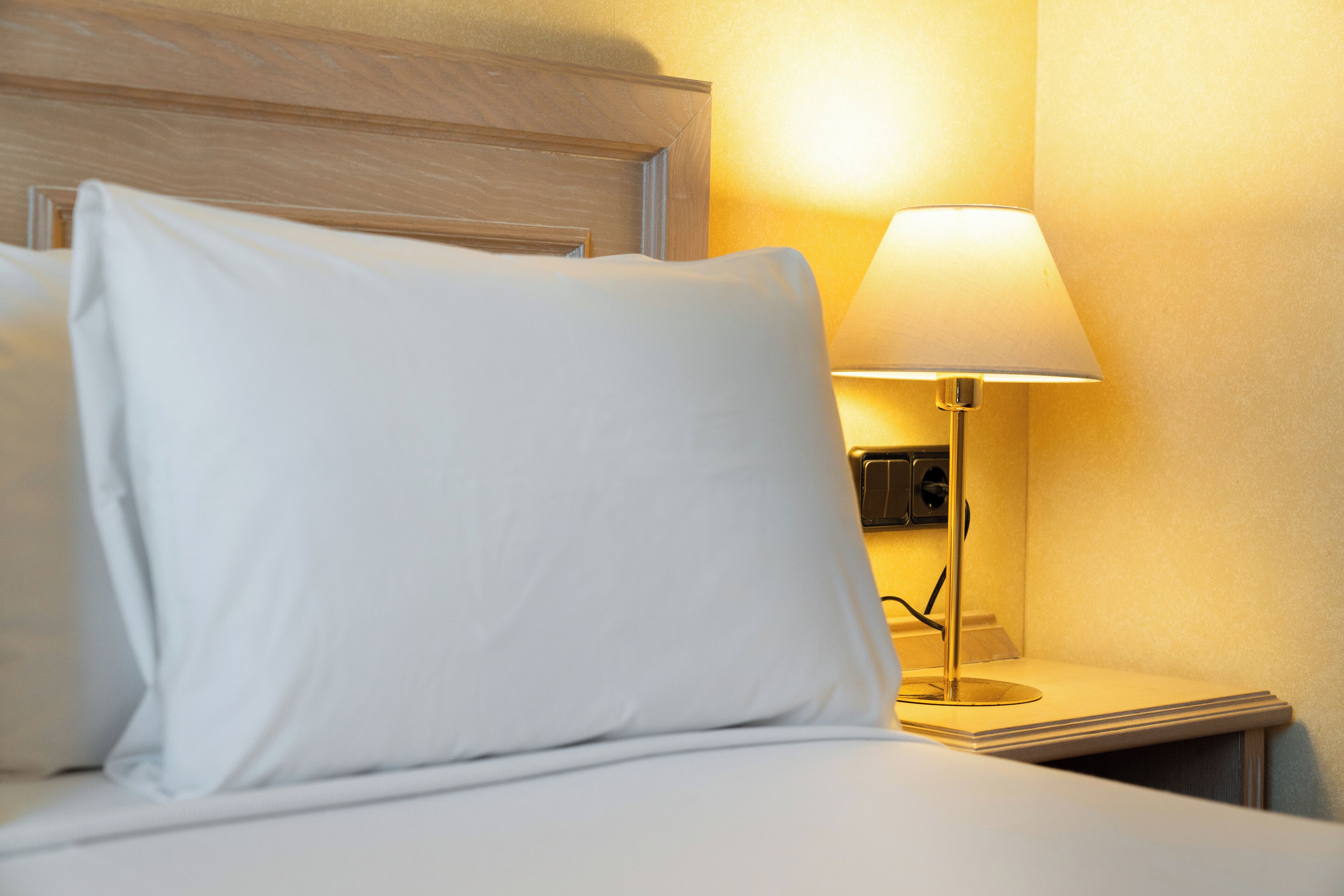 Una cama bien hecha con ropa blanca y una lámpara de noche.