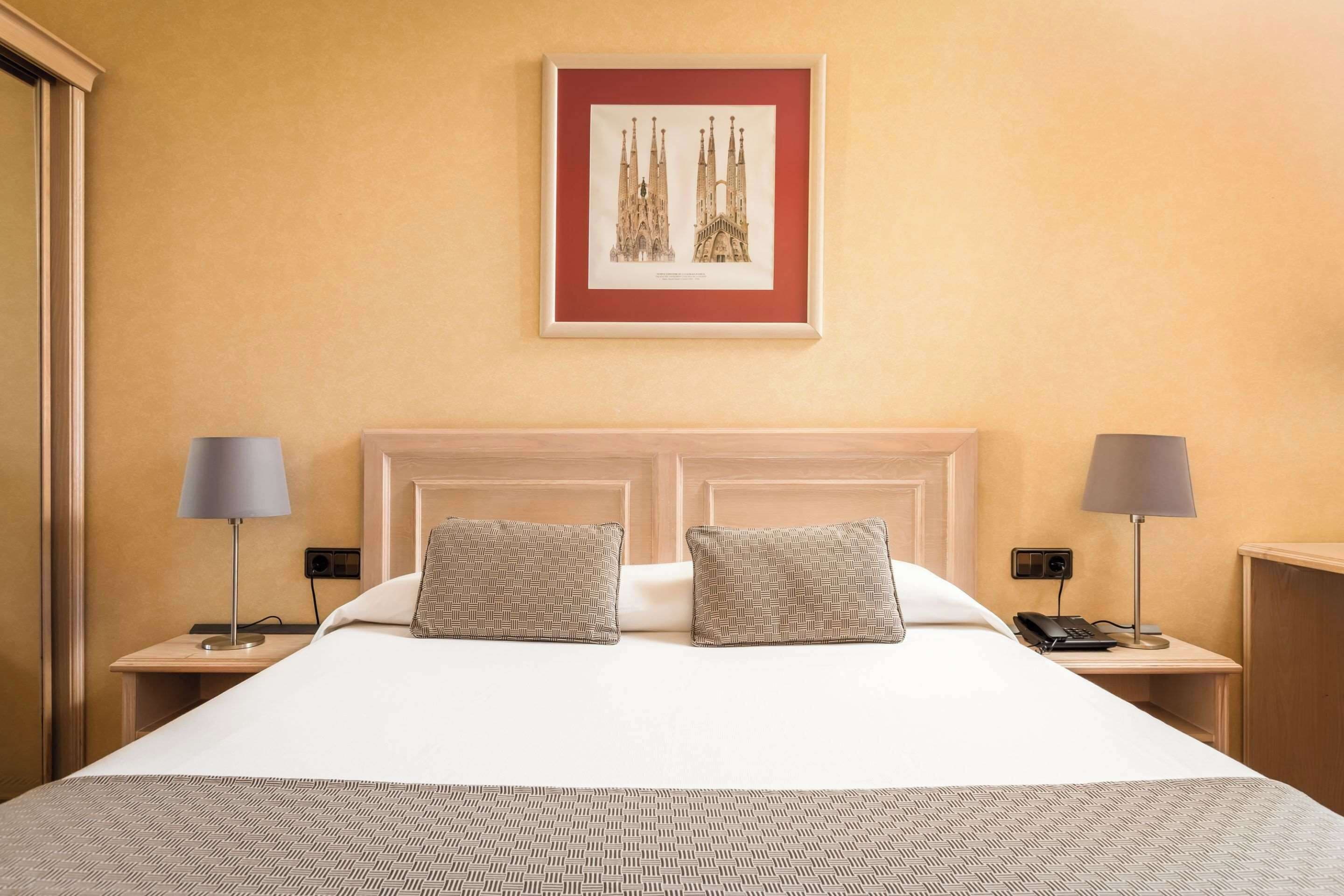A hotel room with a large bed, two nightstands, a framed picture of a cathedral, and a plain wall.