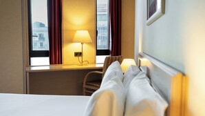 A hotel room with a bed, a desk, a lamp, and a window with curtains. - Petit Palace Junior formerly known as Sunotel Junior (Barcelona)