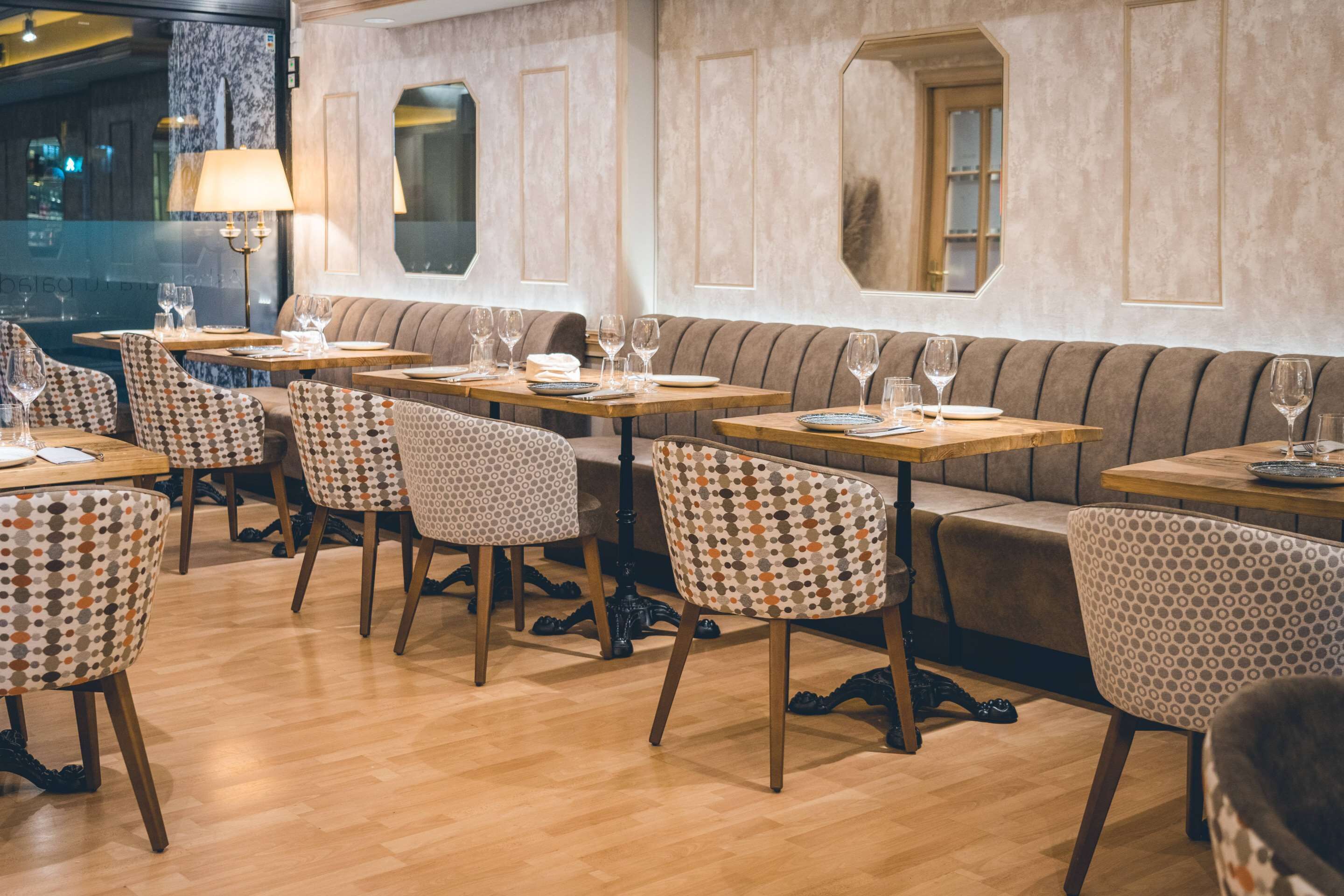 Un interior de restaurante con mesas de madera, sillas estampadas y un banco acolchado.