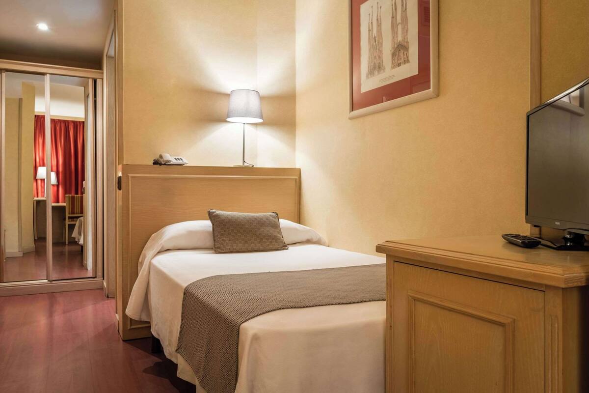 A hotel room with a bed, a bedside lamp, a television, and a door leading to a closet.