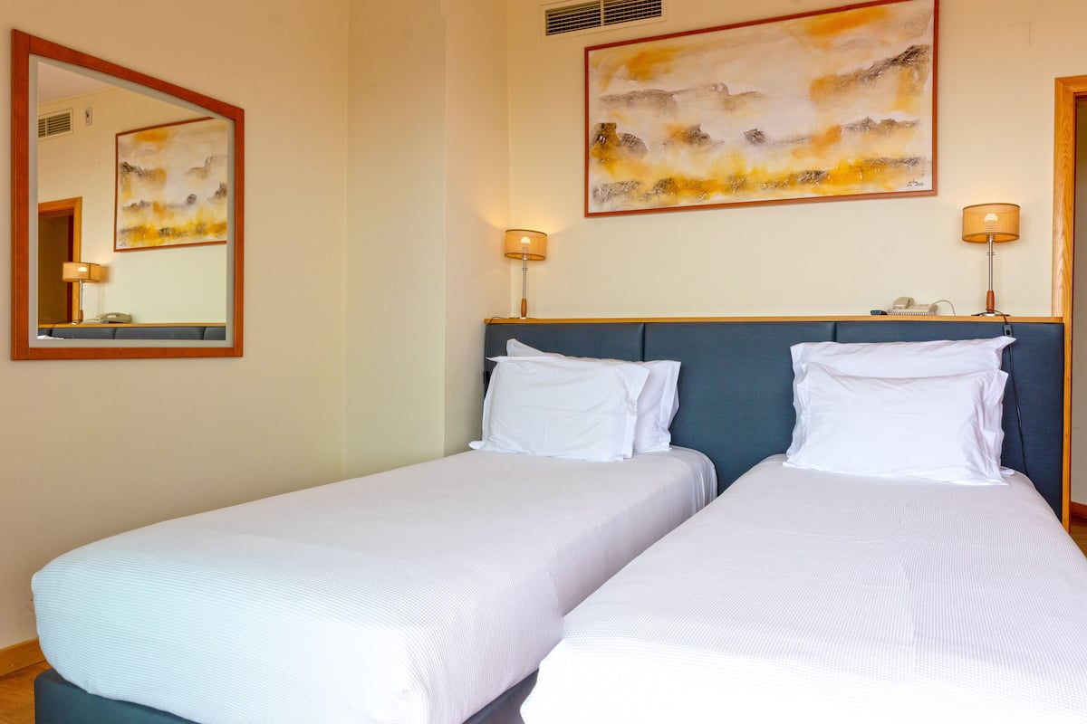 Une chambre d’hôtel avec deux lits simples, un grand miroir, deux lampes fixées au mur et une porte en bois.
