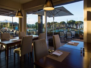 An indoor dining area with tables and chairs, large windows, and an outdoor view. - MS Aparthotel (Oeiras)
