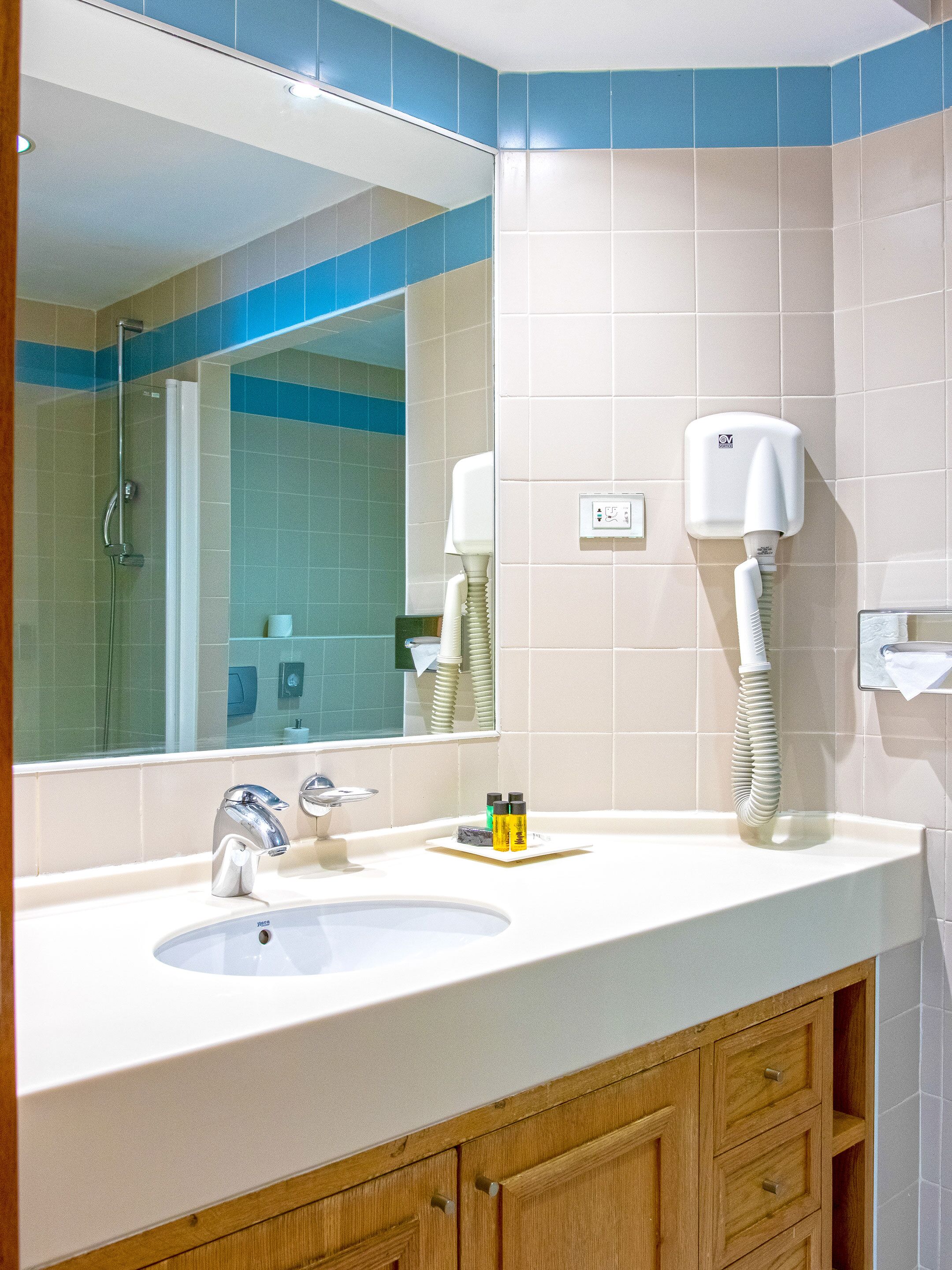Une salle de bain avec un lavabo blanc, un miroir, une douchette à main et un sèche-cheveux fixé au mur.