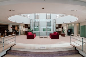 A spacious lobby with a central glass enclosure, red seating, and a staircase leading to upper floors.